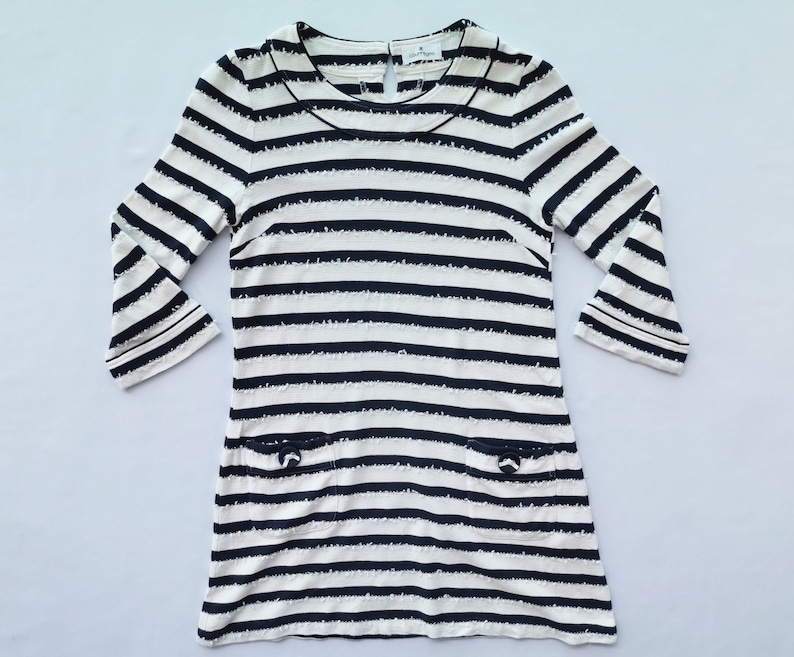 Puede incluir: Vestido color crema con rayas horizontales azul marino. Tiene mangas tres cuartos, cuello redondo y dos peque&ntilde;os bolsillos con detalles de lazo. El vestido mide aproximadamente 86 cm de largo.