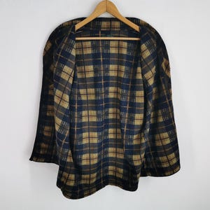 Puede incluir: Una capa vintage con un patr&oacute;n de cuadros en azul marino y marr&oacute;n. La capa est&aacute; colgada en una percha de madera sobre un fondo blanco. El dise&ntilde;o de cuadros es visible tanto en el exterior como en el interior de la capa.