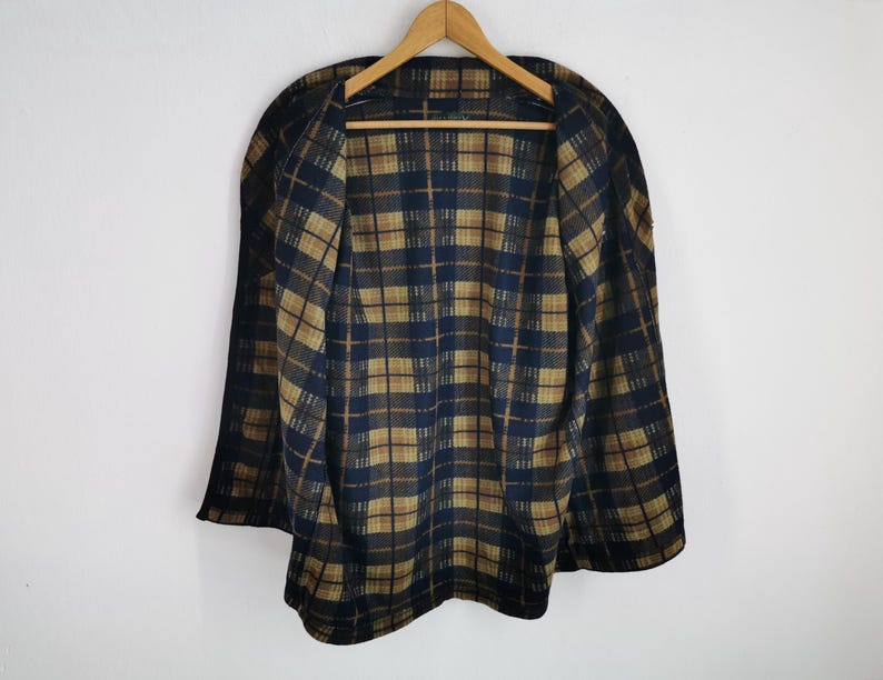 Puede incluir: Una capa vintage con un patr&oacute;n de cuadros en azul marino y marr&oacute;n. La capa est&aacute; colgada en una percha de madera sobre un fondo blanco. El dise&ntilde;o de cuadros es visible tanto en el exterior como en el interior de la capa.
