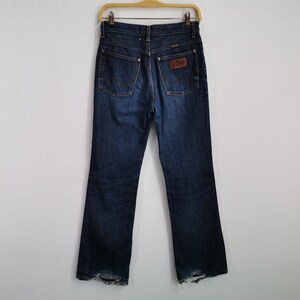 May include: Dark wash denim jeans with a classic five-pocket design, hanging on a wooden hanger. The jeans feature a brown leather patch with the brand name and a faded, worn look at the bottom of the legs.
