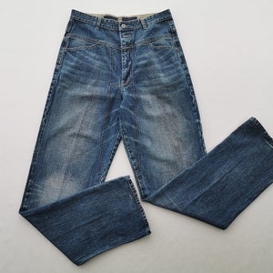 May include: Blue denim jeans with a high waist and button closure. The jeans feature a classic five-pocket design and a straight leg. The denim has a faded wash and subtle distressing.