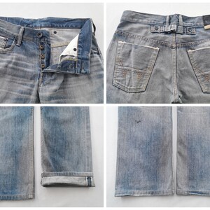 K&ouml;nnte beinhalten: Verblasste blaue Jeans mit Knopfleiste und einem einzigartigen Detail am hinteren G&uuml;rtel. Die Jeans haben ein klassisches F&uuml;nf-Taschen-Design mit sichtbaren N&auml;hten und einem Used-Look. Die Manschetten sind hochgekrempelt.