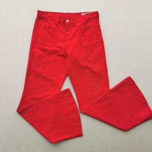 May include: Bright red flared pants with two front pockets and a button closure. The pants have a high waist and a wide leg opening. The fabric appears to be a medium-weight material. The pants are laid flat on a light gray surface.