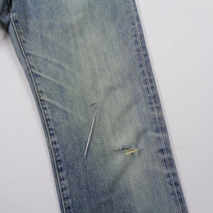 Pu&ograve; includere: Jeans di denim blu sbiadito con un aspetto usurato. I jeans presentano un aspetto vissuto con un piccolo strappo nella zona del ginocchio. Il denim ha un lavaggio chiaro e un classico design a cinque tasche.