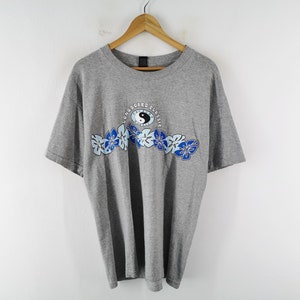 May include: A heather gray short-sleeve t-shirt featuring a graphic print of blue hibiscus flowers and a central yin-yang symbol. The text "LONGBOARD CLASSIC" is printed in a circular arc above the yin-yang icon on the chest area.
