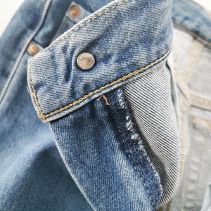 Puede incluir: Primer plano del cuello de una chaqueta vaquera. La chaqueta es de color azul claro con un bot&oacute;n met&aacute;lico y costuras amarillas. El forro interior es de mezclilla azul claro.