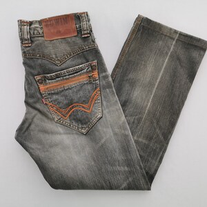 May include: Gray denim jeans with orange stitching and accents. The jeans feature a classic five-pocket design, a leather patch with the brand name "Edwin", and a zip fly. The back pockets have a unique orange stitched design.