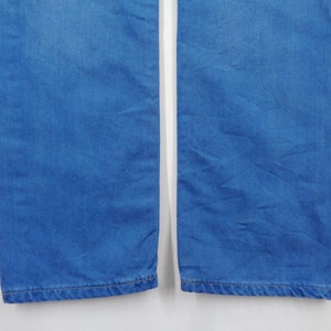 K&ouml;nnte beinhalten: Nahaufnahme des unteren Teils einer blauen Jeans. Der Denim-Stoff hat eine einfarbige, mittelblaue Farbe. Das Bild zeigt die Beine der Jeans mit den S&auml;umen unten. Der Hintergrund ist schlicht wei&szlig;.