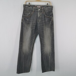 May include: A pair of gray denim jeans hanging on a wooden hanger. The jeans have a faded appearance with visible wear marks and orange stitching. The jeans have a classic five-pocket design and a button and zipper closure.