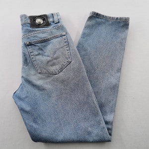 May include: Light blue denim jeans with a classic five-pocket design. Features a leather patch with a logo on the back waistband. The jeans are faded and have a straight leg cut.