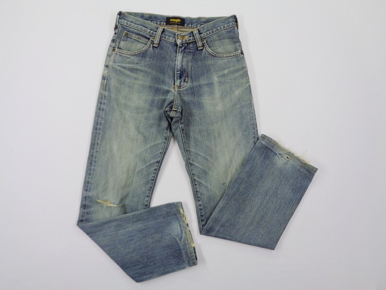 Pu&ograve; includere: Jeans in denim blu chiaro con un lavaggio sbiadito e un aspetto invecchiato. I jeans hanno un classico design a cinque tasche, una chiusura con bottone e cerniera e il logo Wrangler sulla tasca posteriore. I jeans presentano un piccolo strappo sul ginocchio sinistro.