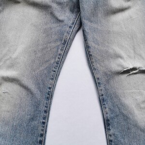 May include: Light blue denim jeans with distressed details, including a tear on the right knee. The jeans have a faded wash and visible stitching along the seams. The image shows the upper portion of the jeans.