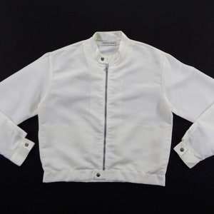 May include: A white jacket with a stand-up collar and a full-length zipper. The jacket has long sleeves with buttoned cuffs and a button closure at the waist. The jacket appears to be made of a lightweight material.