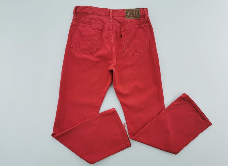 Op de afbeelding: Felrode denim jeans met een klassiek ontwerp met vijf zakken. De jeans hebben een rechte pijp en een leren merkpatch op de rug. Het merk Edwin is zichtbaar op de patch.