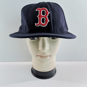 May include: A navy blue baseball cap with a red and white embroidered "B" logo on the front. The cap has a flat brim and a structured crown. The hat is displayed on a mannequin head.