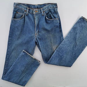 May include: Light blue denim jeans with a classic five-pocket design. The jeans have a button and zipper closure, belt loops, and a faded wash. The straight-leg style is visible, and the jeans are laid flat on a white surface.