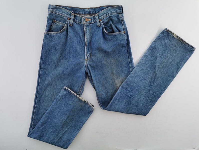 May include: Light blue denim jeans with a classic five-pocket design. The jeans have a button and zipper closure, belt loops, and a faded wash. The straight-leg style is visible, and the jeans are laid flat on a white surface.