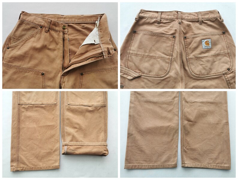 May include: Close-up shots of tan work pants. The pants have multiple pockets, reinforced stitching, and a button and zipper closure. The Carhartt logo is visible on the back pocket. The cuffs are folded up on one leg.