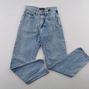 May include: Light blue denim jeans with a classic five-pocket design. The jeans have a straight leg cut and a button and zipper closure. The brand name is visible on the back waistband. The jeans are laid flat on a light gray surface.