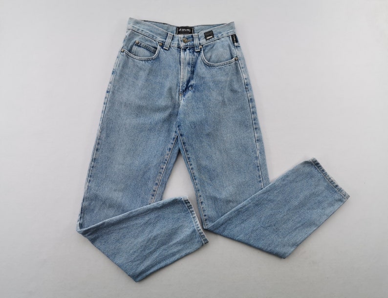 May include: Light blue denim jeans with a classic five-pocket design. The jeans have a straight leg cut and a button and zipper closure. The brand name is visible on the back waistband. The jeans are laid flat on a light gray surface.