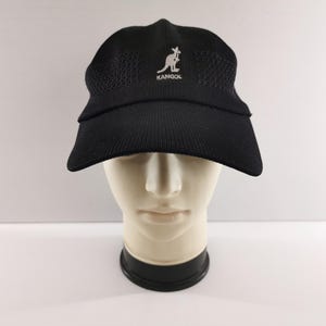Puede incluir: Gorra Kangol negra con visera curva, exhibida en una cabeza de maniqu&iacute;. La gorra presenta el logotipo de Kangol en blanco. La gorra est&aacute; hecha de un material texturizado y transpirable.
