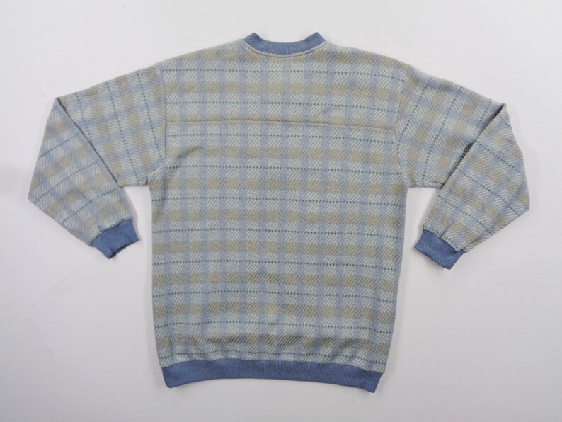 Puede incluir: Sudadera con estampado de cuadros en azul claro y beige con pu&ntilde;os, cuello y dobladillo azules. La parte superior de manga larga tiene cuello redondo y un aspecto suave y texturizado. La parte posterior de la camisa es visible.