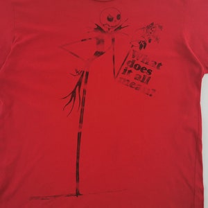 May include: Red t-shirt featuring a black graphic of Jack Skellington from The Nightmare Before Christmas. The design includes Jack's tall, thin figure and the text "What does it all mean?"