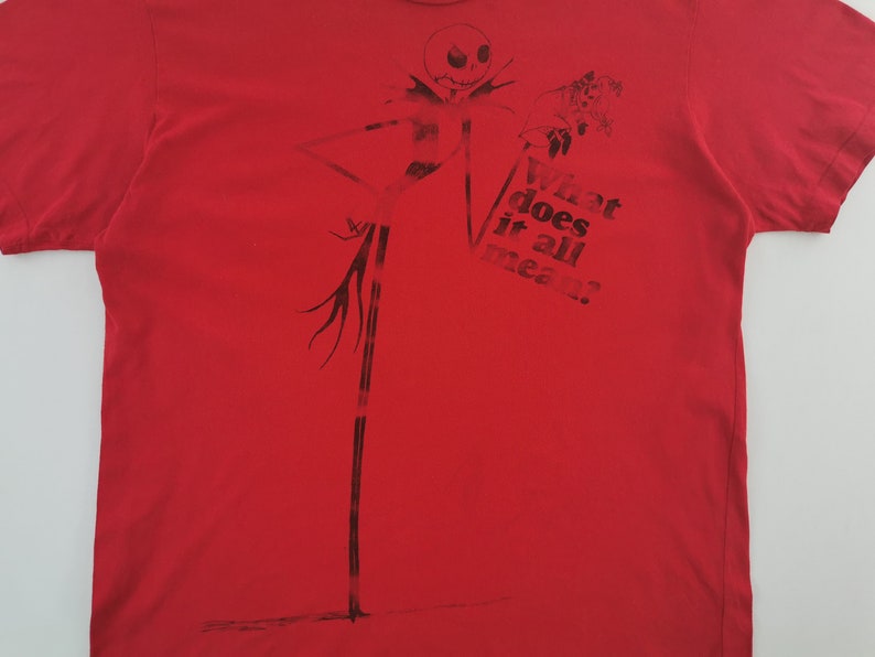 May include: Red t-shirt featuring a black graphic of Jack Skellington from The Nightmare Before Christmas. The design includes Jack's tall, thin figure and the text "What does it all mean?"