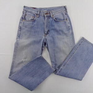 May include: Light blue denim jeans with a classic five-pocket design. The jeans have a faded wash and a distressed detail on the front. The jeans are folded and laid flat on a white surface.