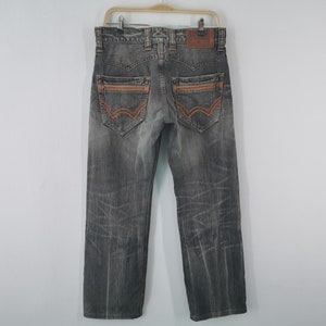 May include: Gray denim jeans with orange stitching accents on the back pockets and seams. The jeans are hanging on a wooden hanger against a white background. The jeans have a faded, worn look.