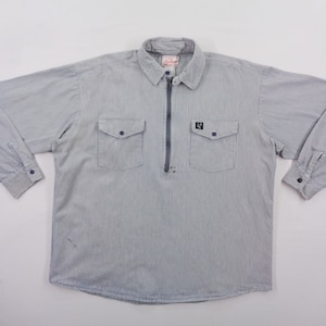 Puede incluir: Camisa de manga larga a rayas azules y blancas, con cuello y cierre de cremallera de cuarto. Tiene dos bolsillos en el pecho y puños abotonados. Un pequeño logotipo es visible en el pecho derecho.