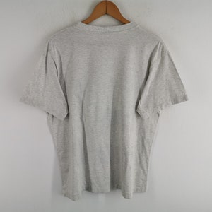 May include: A grey t-shirt hanging on a wooden hanger. The short-sleeved shirt is made of a soft material and has a crew neck. The shirt is displayed against a plain white background.
