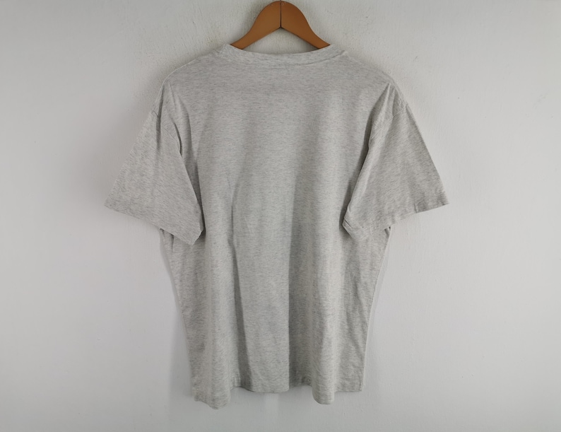 May include: A grey t-shirt hanging on a wooden hanger. The short-sleeved shirt is made of a soft material and has a crew neck. The shirt is displayed against a plain white background.