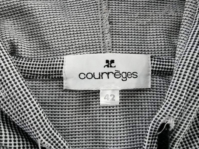 May include: A black and white micro-patterned garment featuring a white rectangular fabric label stitched at the neckline. The label displays the brand name courr&egrave;ges in black lowercase letters with a logo above it and a smaller tag below reading 42.