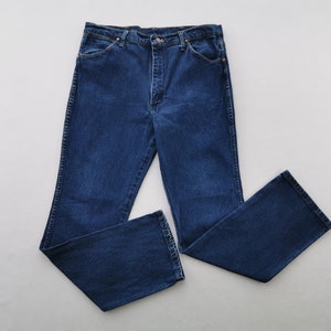 May include: Dark blue denim jeans with a classic five-pocket design. The jeans have a straight leg cut and a button and zipper closure. The fabric appears to be a medium-weight denim, suitable for everyday wear. The jeans are laid flat on a white surface.