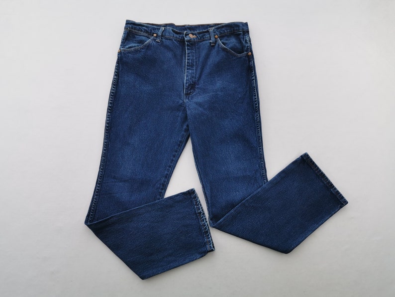 May include: Dark blue denim jeans with a classic five-pocket design. The jeans have a straight leg cut and a button and zipper closure. The fabric appears to be a medium-weight denim, suitable for everyday wear. The jeans are laid flat on a white surface.