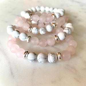 Peut inclure: Quatre bracelets superposés avec des perles blanches et roses alternées. Les bracelets sont faits de perles de howlite blanche et de quartz rose avec des entretoises argentées.