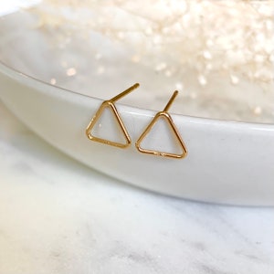 May include: A pair of gold triangle stud earrings. The earrings are simple and minimalist, and they would be a great addition to any jewelry collection.