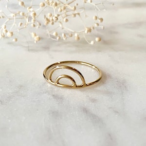 May include: A gold-toned ring with a simple, minimalist rainbow design. The ring is made of metal and has a smooth, polished finish.