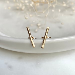 May include: A pair of gold hammered bar stud earrings. The earrings are simple and minimalist, and they would make a great everyday accessory.