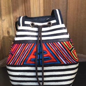 May include: A black and white striped drawstring bag with a colorful geometric pattern in the center. The bag has a brown drawstring and two black straps.