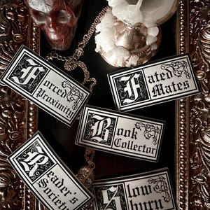 May include: Five black and white stickers with gothic lettering and decorative flourishes. The stickers say "Forced Proximity", "Fated Mates", "Book Collector", "Reader's Society", and "Slow Burn".