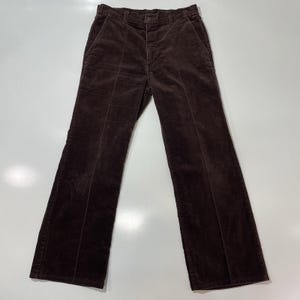 May include: Brown corduroy trousers. These trousers feature a classic five-pocket design with a button and zip fastening. The corduroy fabric has a soft, velvety texture and a subtle sheen. The trousers have a flared leg opening.