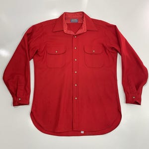 May include: A long-sleeved red shirt with two chest pockets and a collared neckline. The shirt has a button-down front and buttoned cuffs. The shirt is made of a solid red fabric.