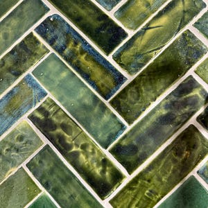 Può includere: Primo piano di un motivo a spina di pesce di piastrelle in ceramica verdi e verde-blu. Le piastrelle sono rettangolari con finitura lucida e sono disposte a motivo diagonale con fughe bianche. Le variazioni di colore creano un aspetto strutturato.