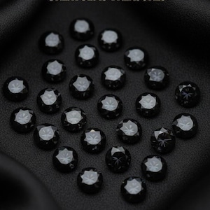 Puede incluir: Primer plano de una colección de gemas negras redondas con superficies facetadas, dispuestas sobre tela oscura. El texto "GREATGEMS TREASURES" es visible en la parte superior.