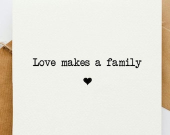 May include: A white card with black text that reads "Love makes a family" with a small black heart below the text.