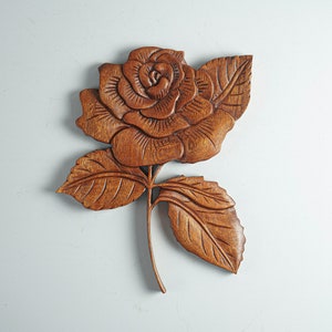 May include: A wooden carving of a rose with intricate details. The rose is brown and has a natural wood finish. The carving is a beautiful example of traditional craftsmanship.