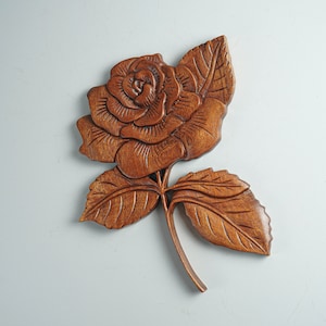 May include: A wooden carving of a rose with brown leaves. The rose is carved in detail and has a realistic appearance.