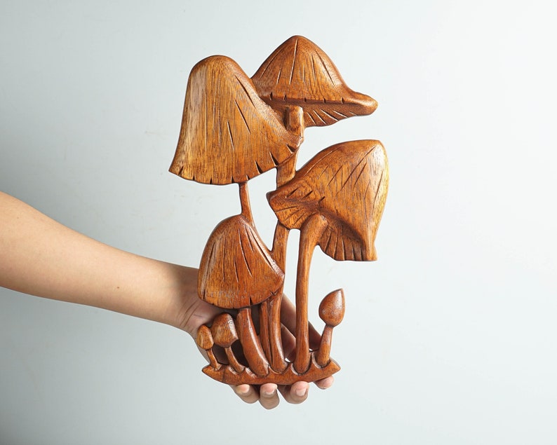 Op de afbeelding: Een handgesneden houten sculptuur met een groep paddenstoelen van verschillende groottes. Het object toont een natuurlijke bruine houtnerf met gedetailleerde verticale inkervingen op de hoeden en stelen, in totaal zes paddenstoelen.